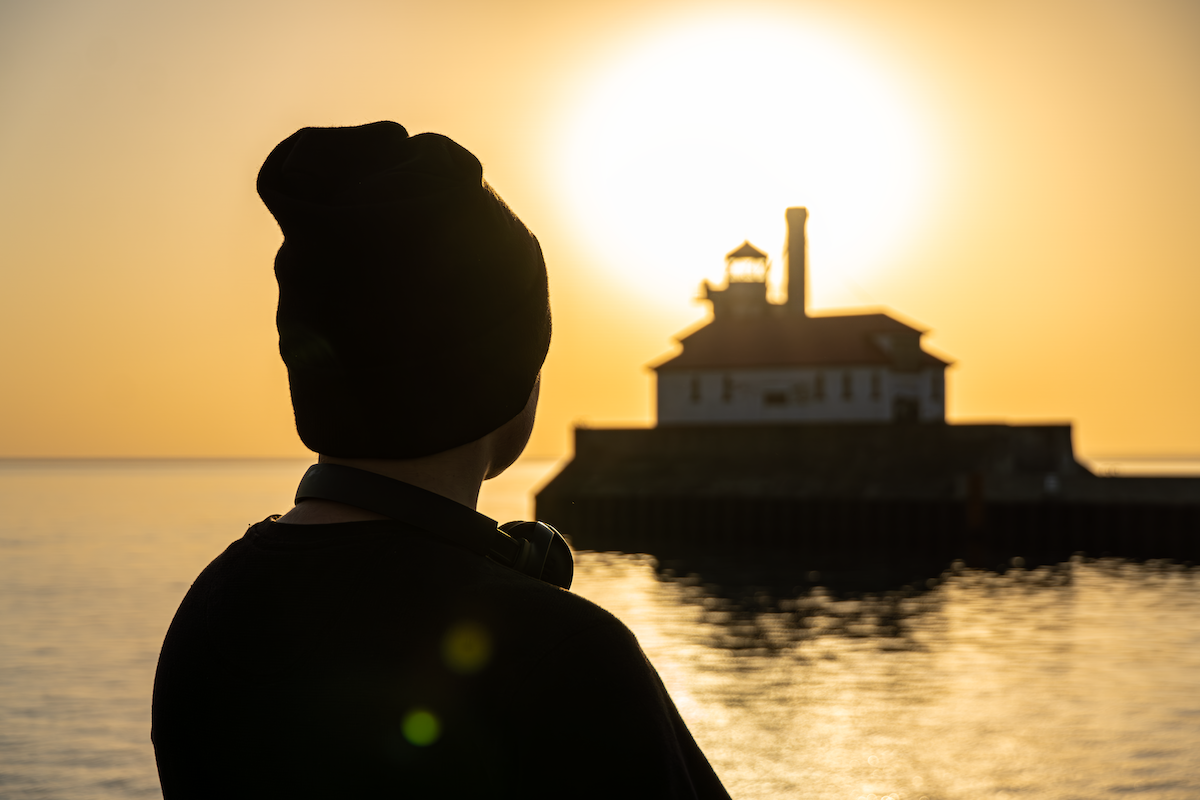 A person looking toward a lighthouse at sunset